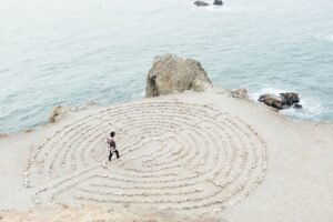 Mental health, behavioral health, Person walking in a seaside labyrinth, symbolizing a therapeutic journey.