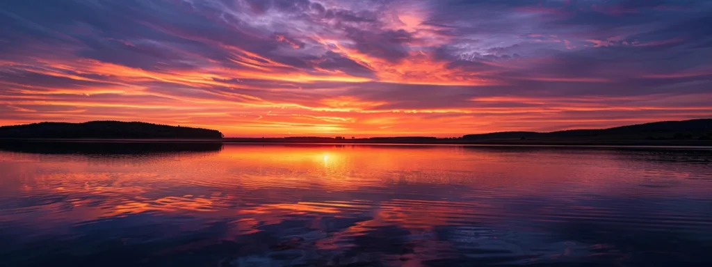a breathtaking sunset casts vibrant hues of orange and purple across a serene lake, with wispy clouds reflecting beautifully on the tranquil water surface.