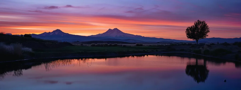 a vibrant sunset casts a warm glow over a tranquil lake, reflecting the fiery hues of orange and pink while silhouetted mountain peaks frame the horizon.