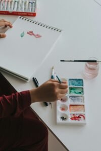 Hand dipping a paintbrush into watercolor paint in soft natural light