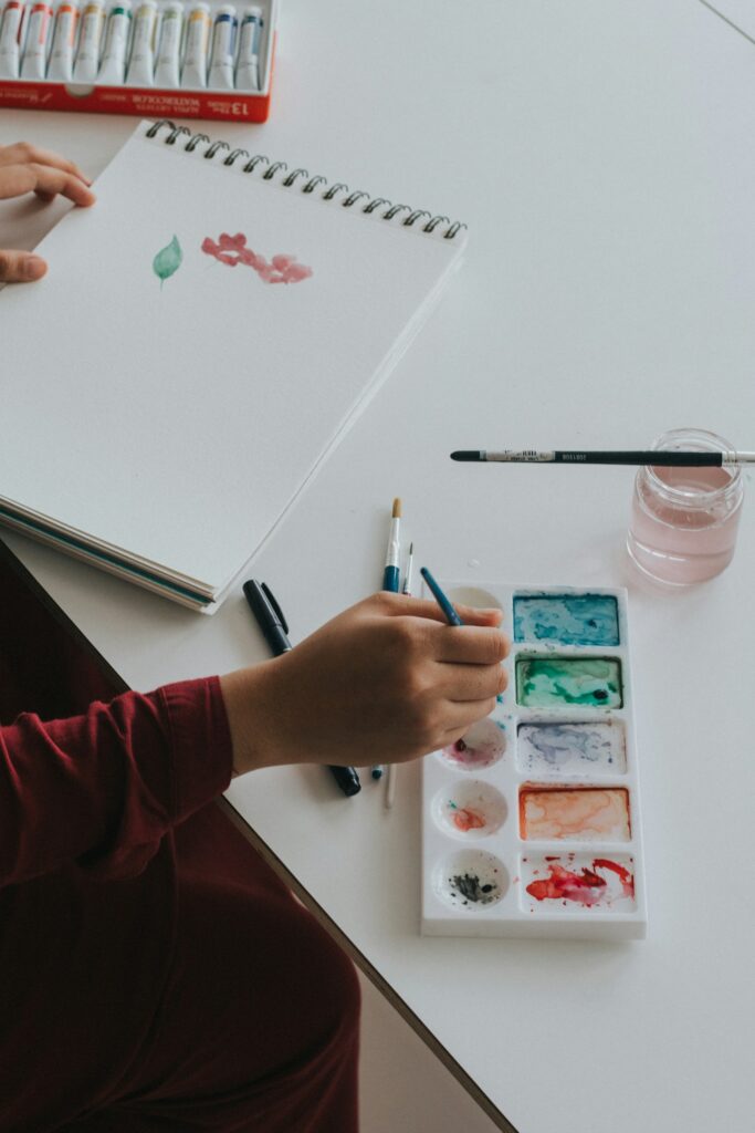 Hand dipping a paintbrush into watercolor paint in soft natural light