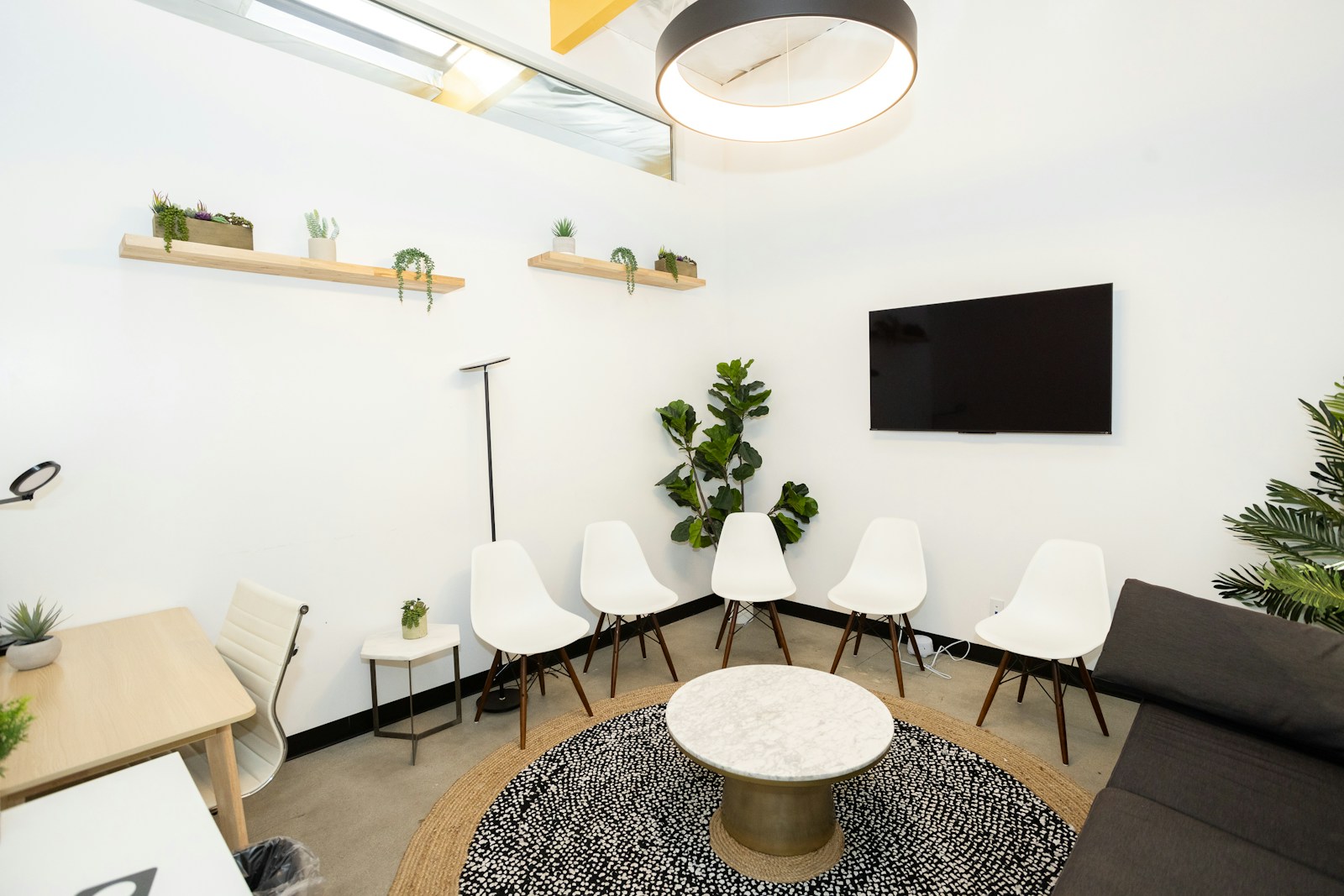 A calm waiting room with white chairs, plants, and natural light