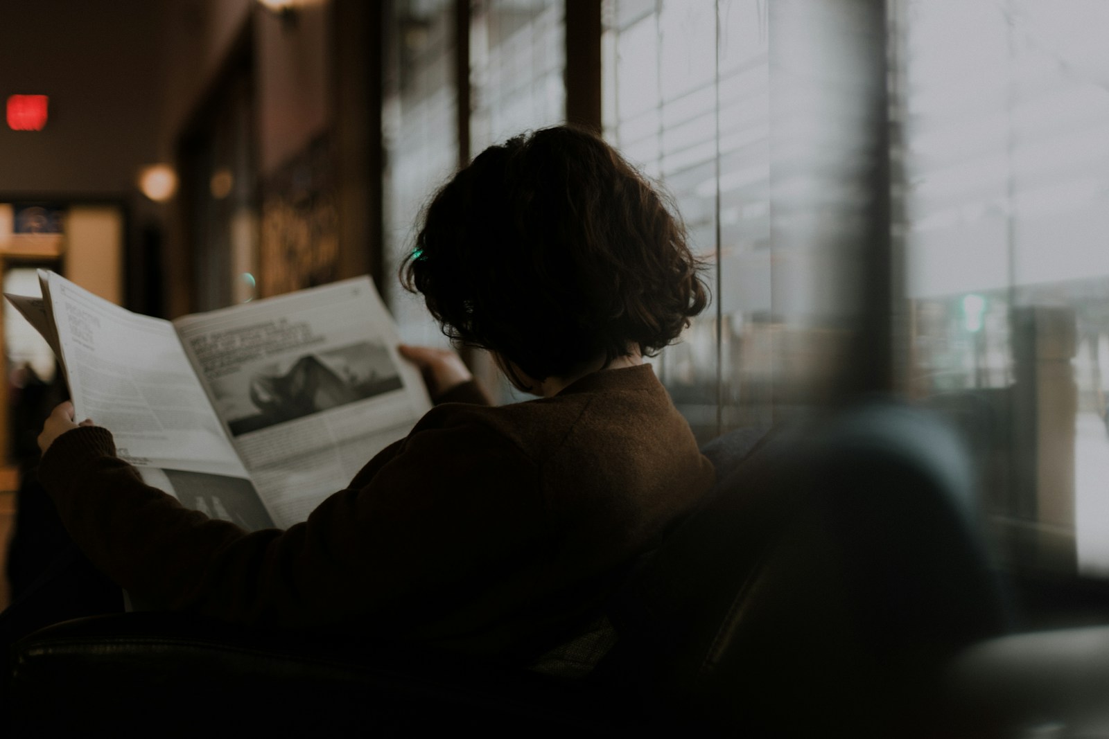 A woman in a brown long-sleeve sweater sitting by a window, looking thoughtful
