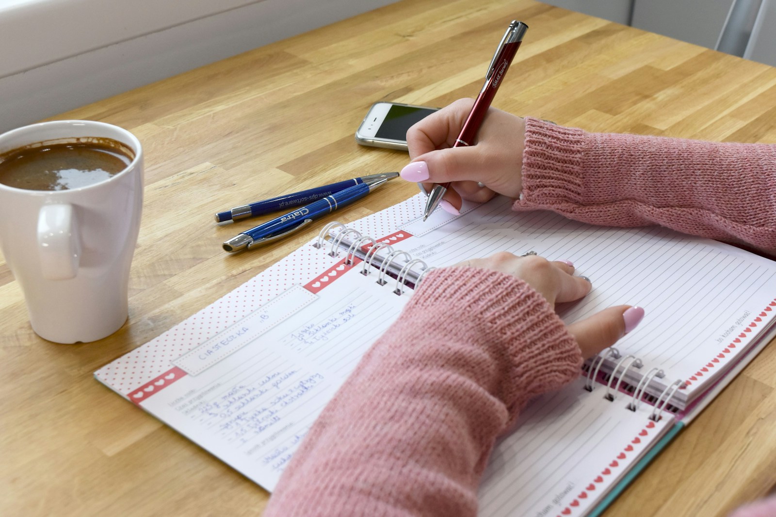 A person writing in a notebook next to a coffee cup in morning light