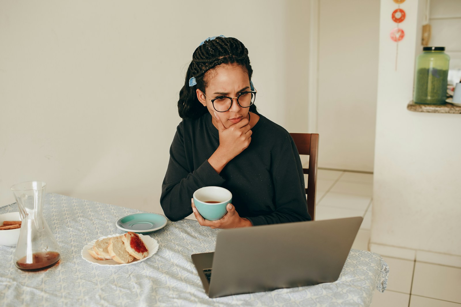 A woman in a black long-sleeve top wearing eyeglasses, looking contemplative