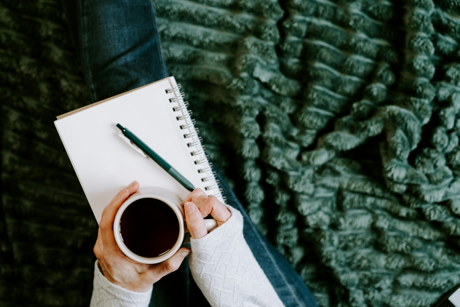 A person holding a coffee cup next to a notebook in quiet morning light