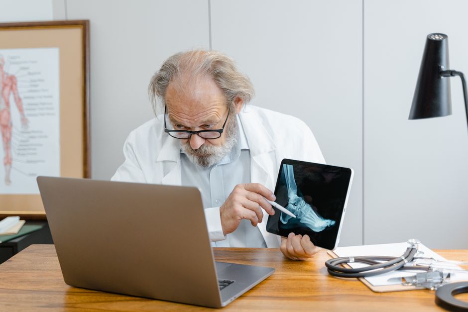 Senior doctor viewing and explaining an ankle X-ray on a tablet during a video consultation.