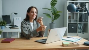 Young female office worker is recording audio message using smartphone in workplace at desk touching screen talking smiling communicating on business.