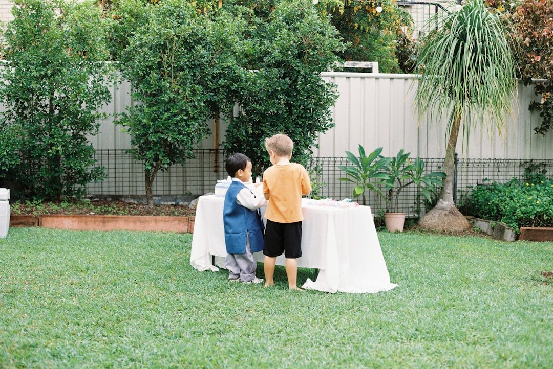 Two young children stand by a table in a backyard.