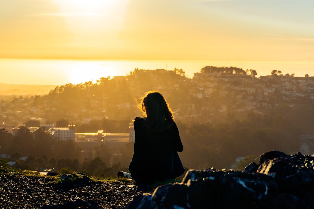 A woman standing on top of a hill with a sunset in the background.