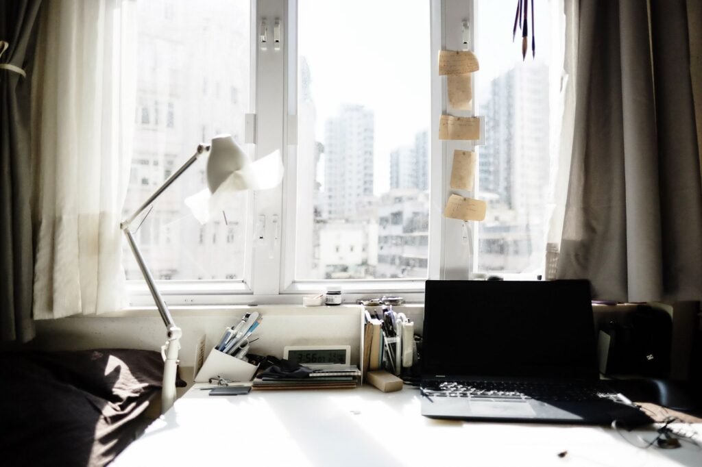 Bright home workspace with a laptop, desk lamp, and city view through large windows.