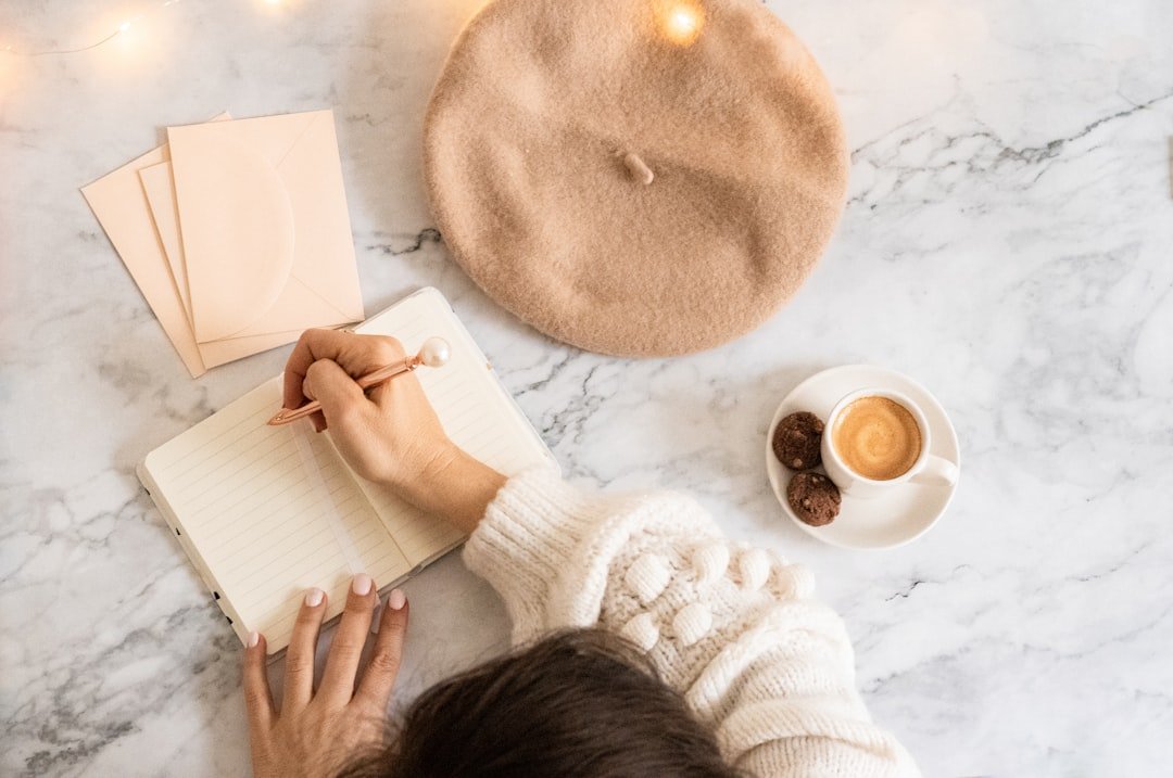 a person writing on a notebook next to a cup of coffee.