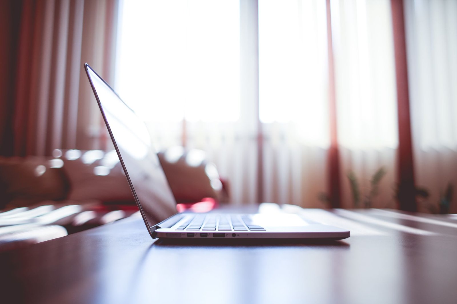 A modern laptop on a table illuminated by soft natural light from nearby windows.