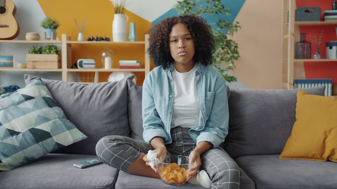How to Choose a Virtual IOP in California: A Decision Guide 6 attractive African-American woman crying over sad drama on TV. Young lady is sitting on comfortable couch and holding remote control and snacks touching face wet eyes with tissue.