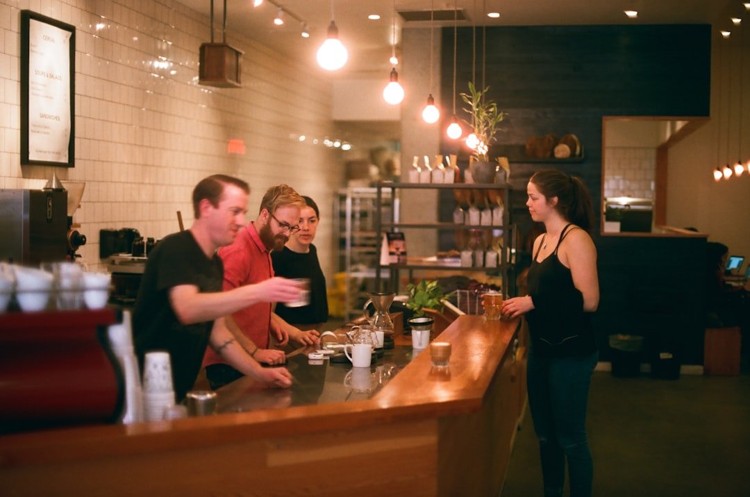 woman in black tank top stands in front of counter with three men inside.