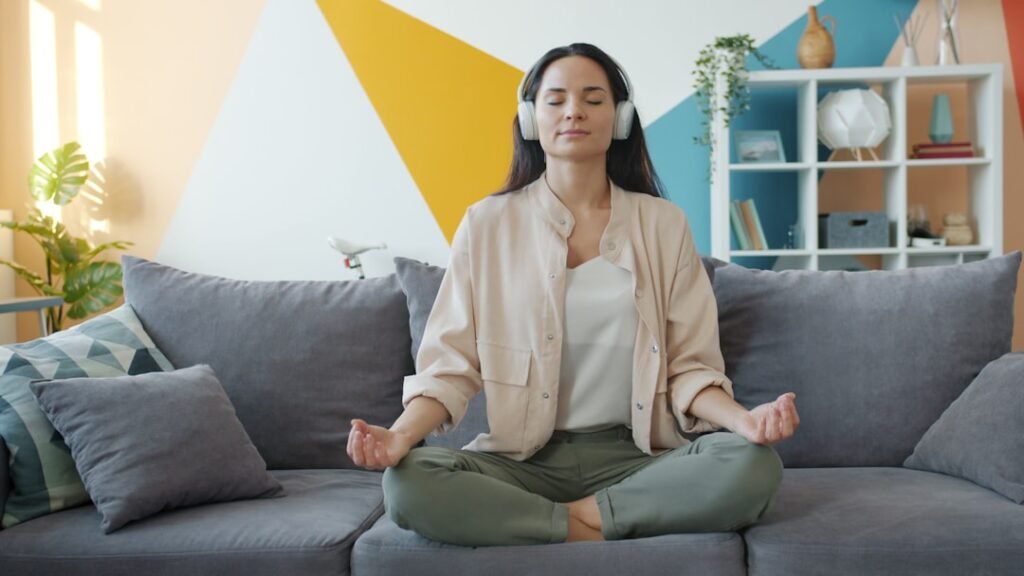 Virtual IOP in Charlotte, North Carolina 1 happy girl in headphones listening to music and relaxing lotus position sitting on sofa in apartment enjoying leisure time and modern technology.