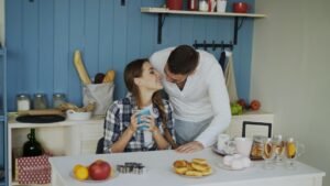 Attractive couple meet and kiss in the kitchen at breakfast time at home in the morning.