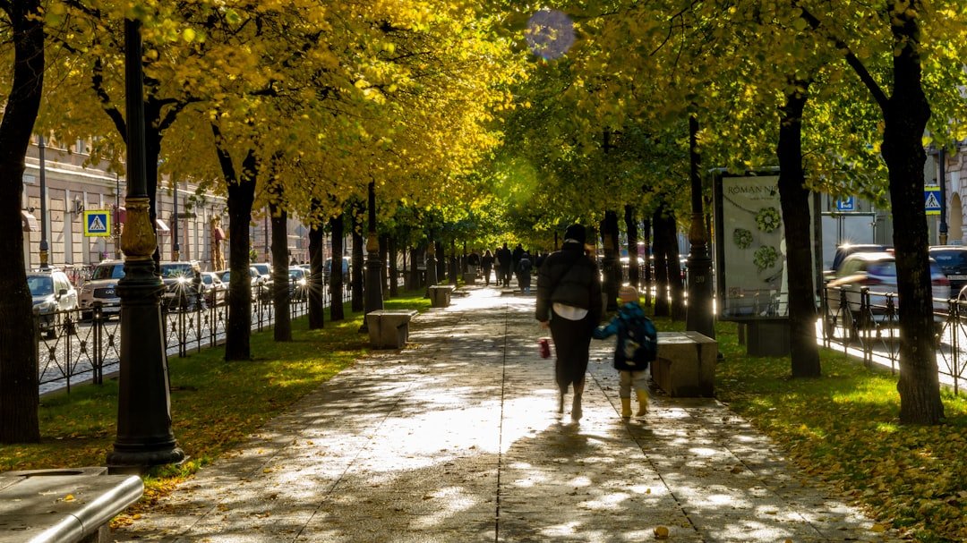 Two people walk down a tree-lined path in autumn.