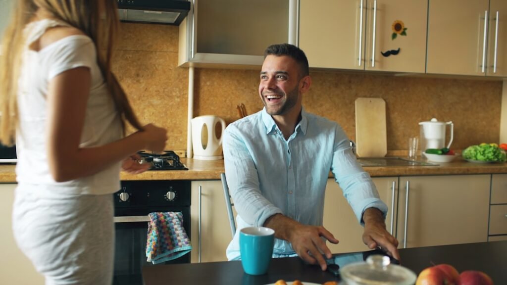 Attractive couple meet in the kitchen early morning kisssing and ebracing then using digital tablet computer for social media surfing at home.