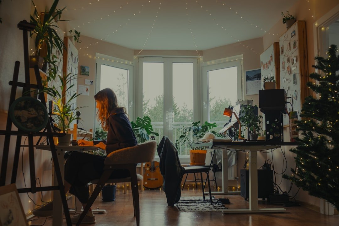 Woman working at a desk in a cozy, plant-filled room.