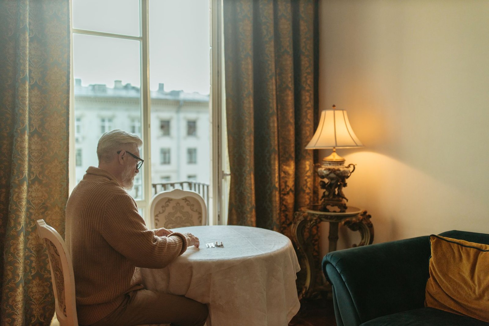A senior man with white hair sits by a table in a vintage room.