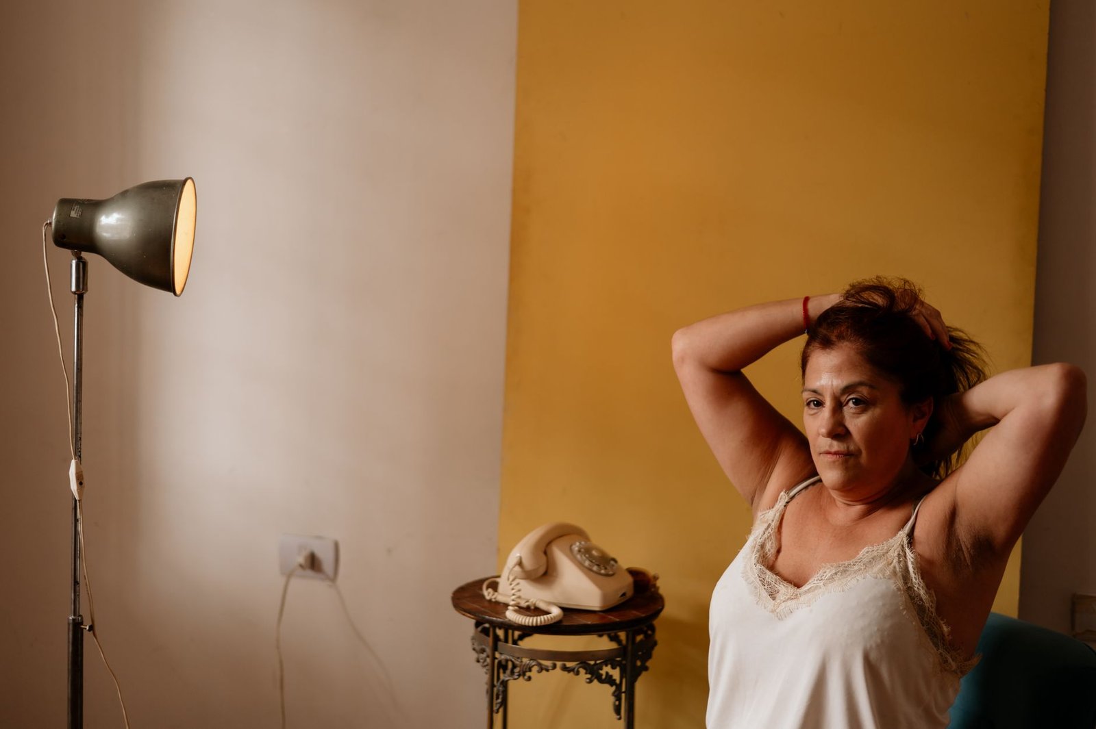A woman sitting relaxed indoors next to a vintage lamp and telephone.