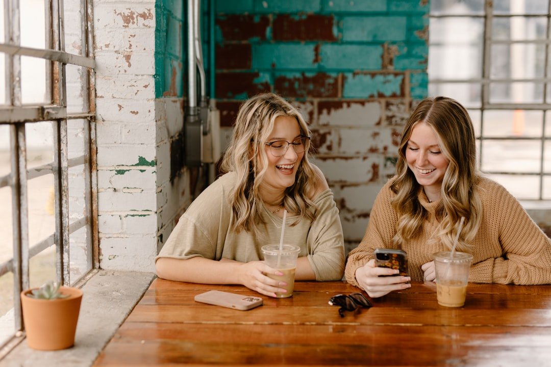 two women sitting at a table looking at a cell phone.