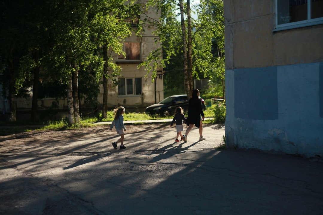 An adult and two children walk on a sunlit path.
