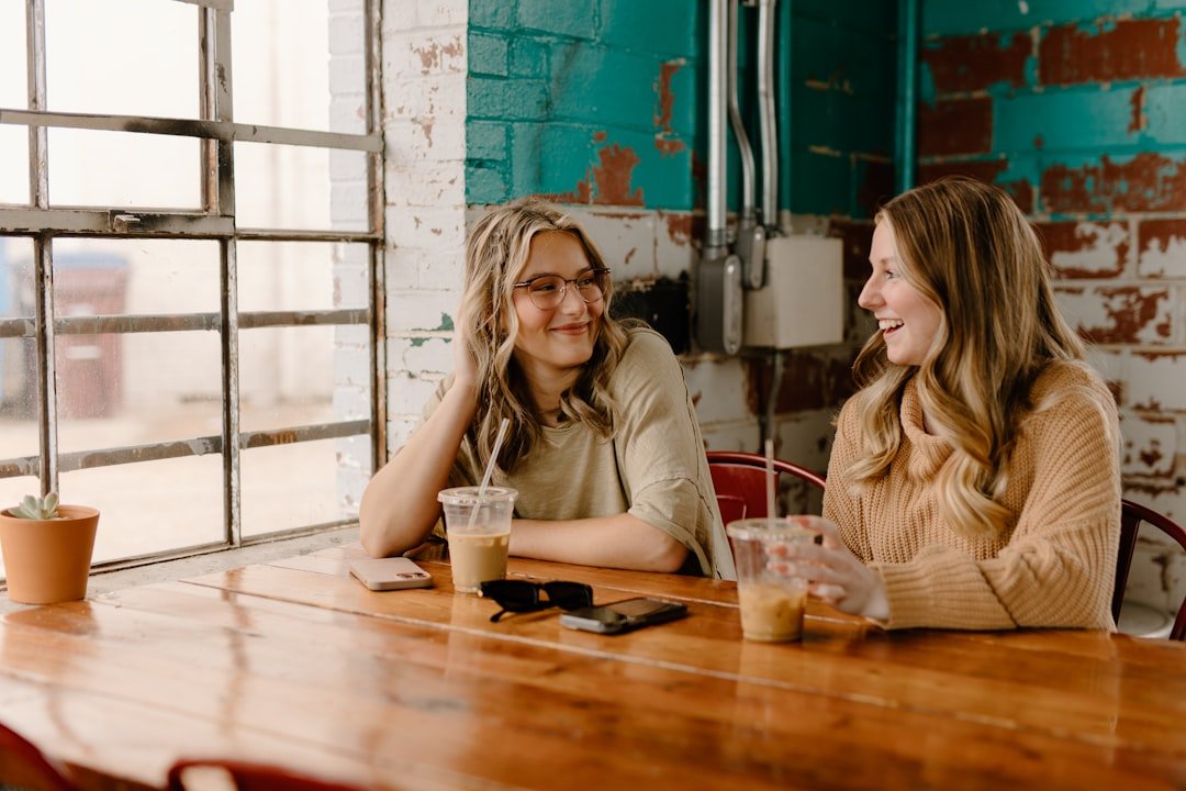 a couple of women sitting at a wooden table.
