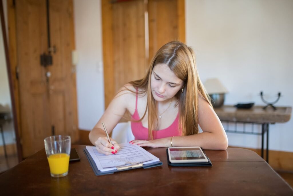 Focused young woman studying indoors with a tablet and orange juice on a wooden table.