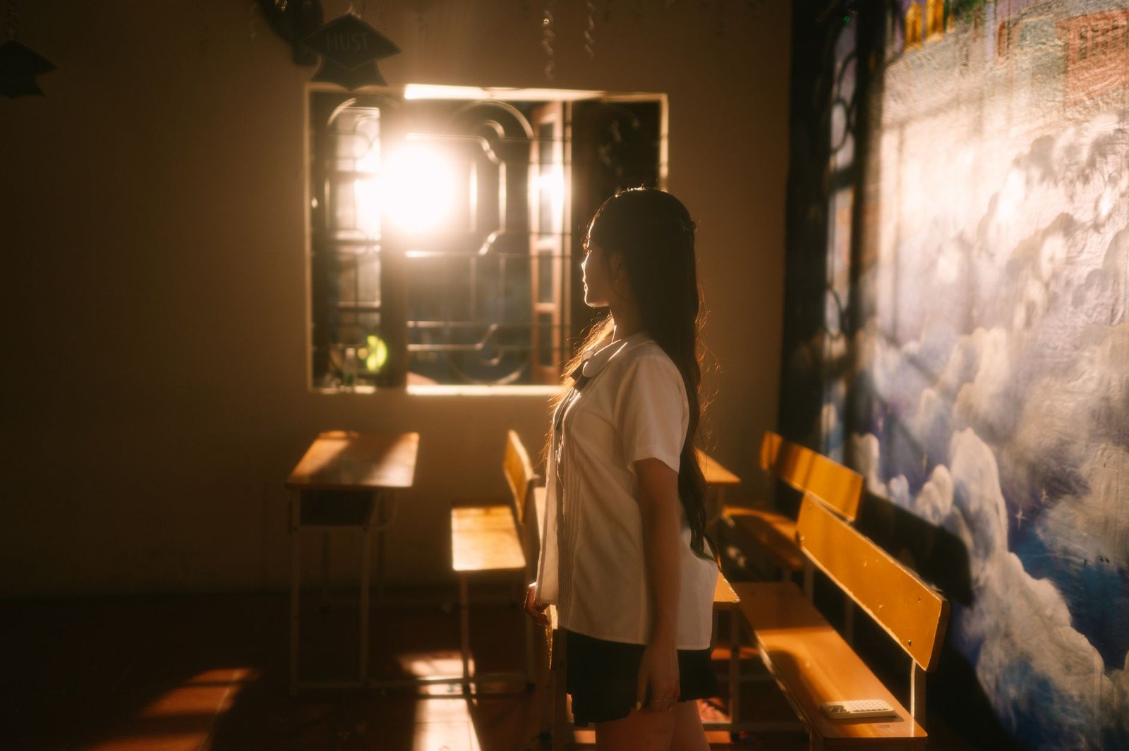 A young woman stands thoughtfully in a warmly lit classroom, evoking a serene and contemplative mood.