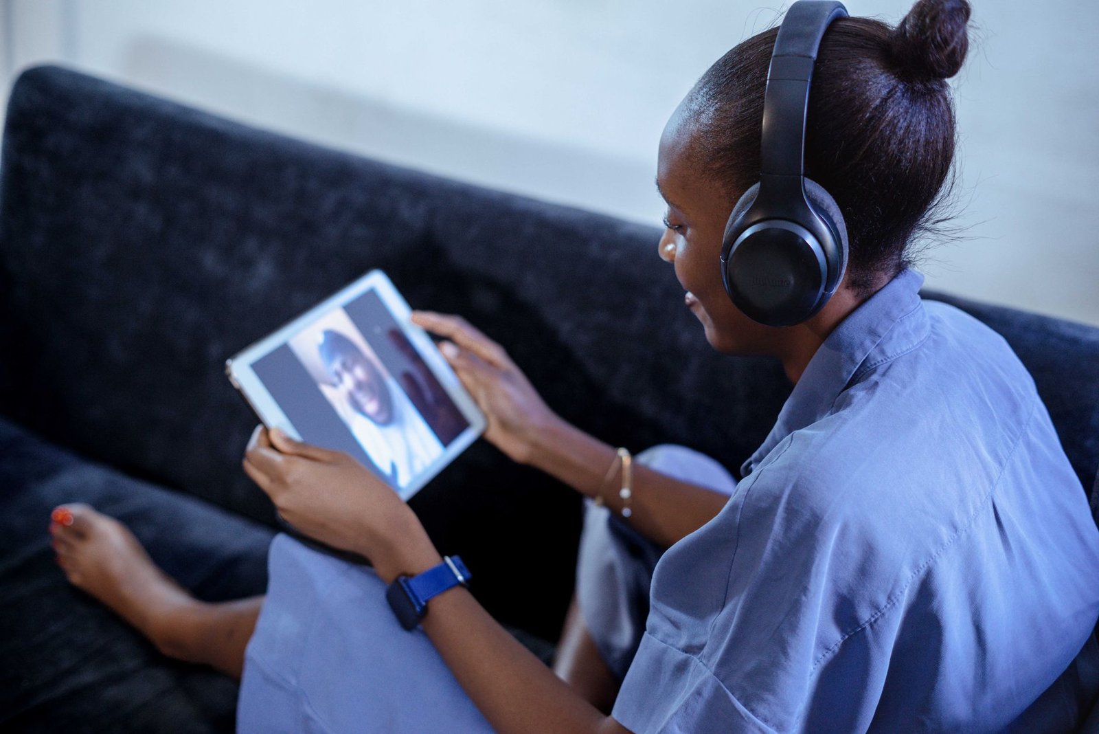 Young woman using tablet for video call on sofa, wearing headphones.