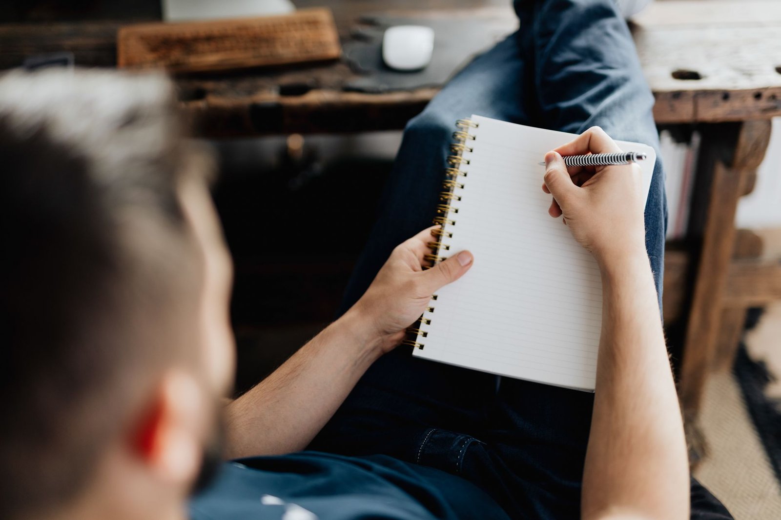 Man lying back and writing on a notebook, relaxing at home. Cozy setting with a rustic desk.