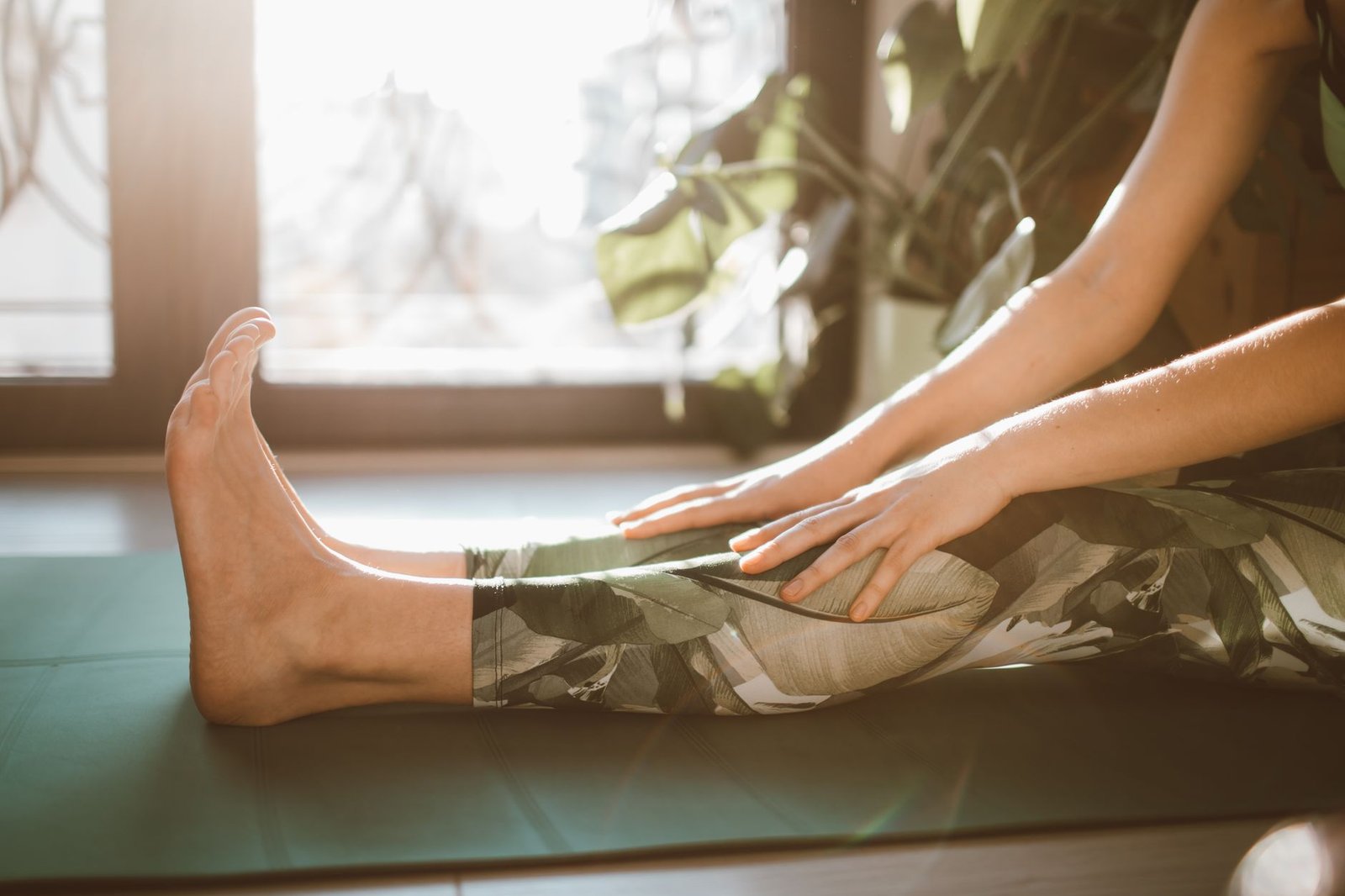 A person stretching on a yoga mat indoors with sunlight streaming through a window.
