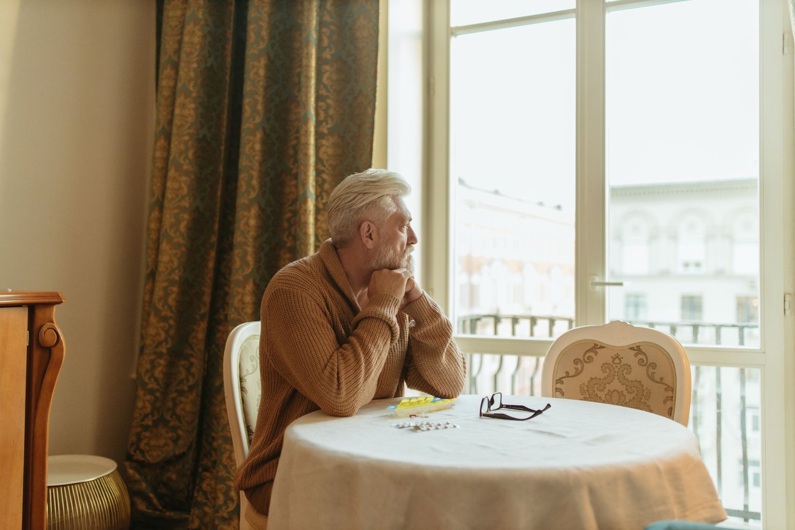 Elderly man in a cozy room gazing thoughtfully out the window during the day.