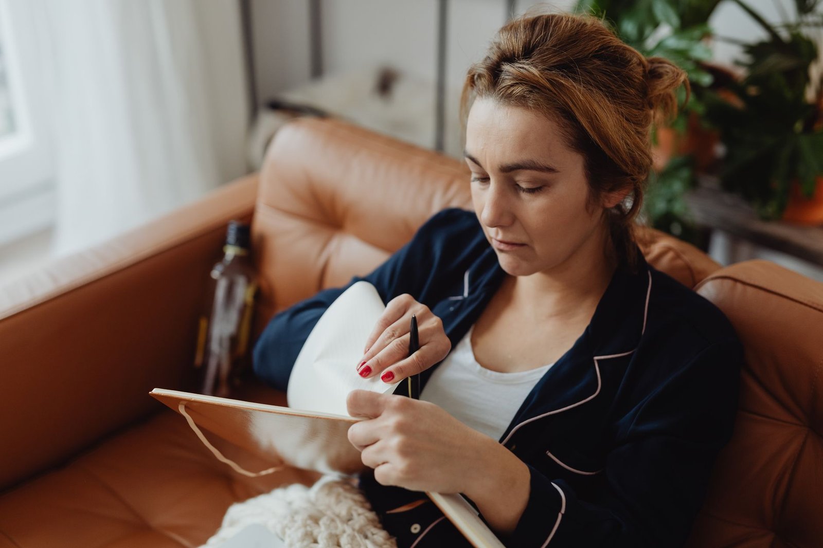Woman relaxing on a sofa, writing in a notebook while wearing pajamas.