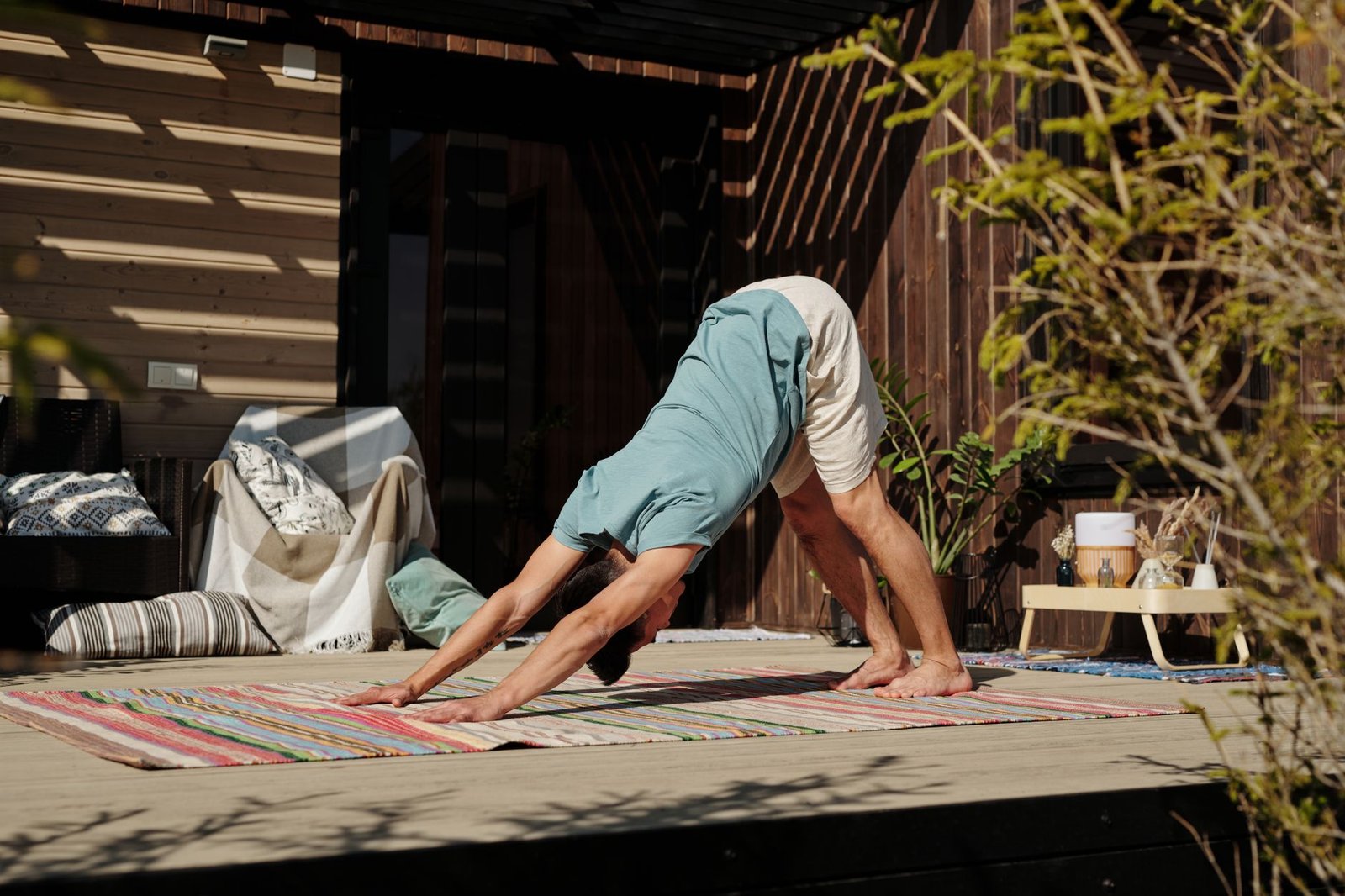 Adult man performing yoga on a veranda under the sun, emphasizing healthy lifestyle and relaxation.
