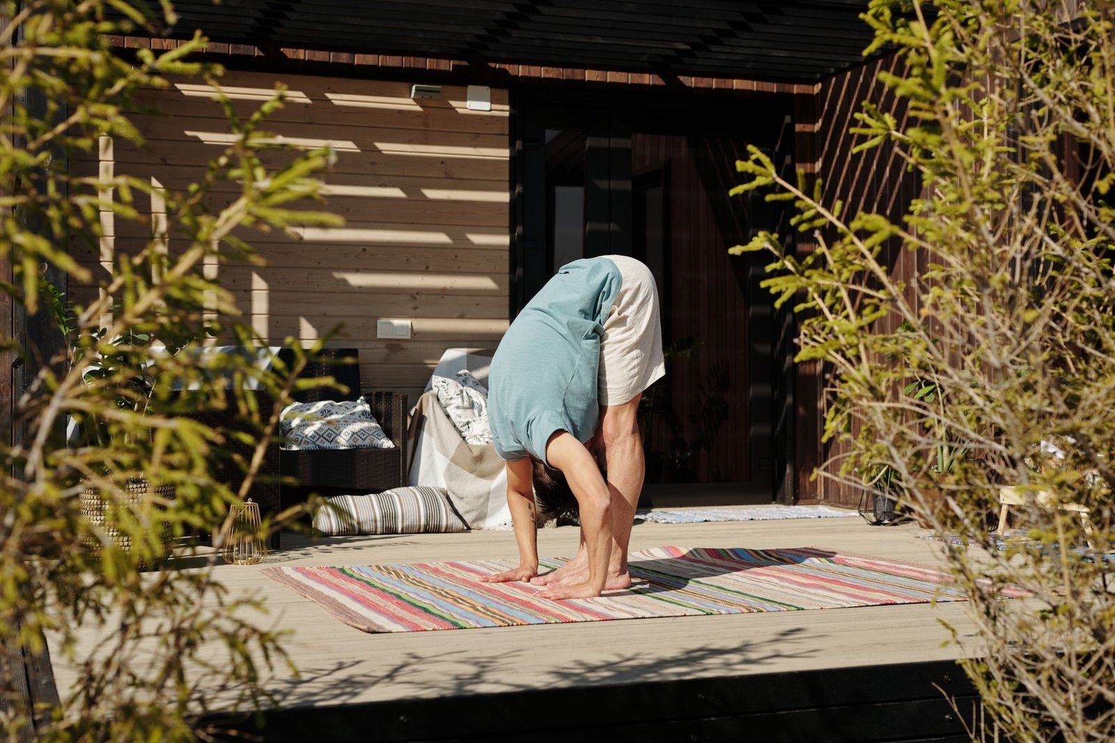 Man practicing yoga outdoors, showcasing a healthy lifestyle through stretching exercises on a veranda.
