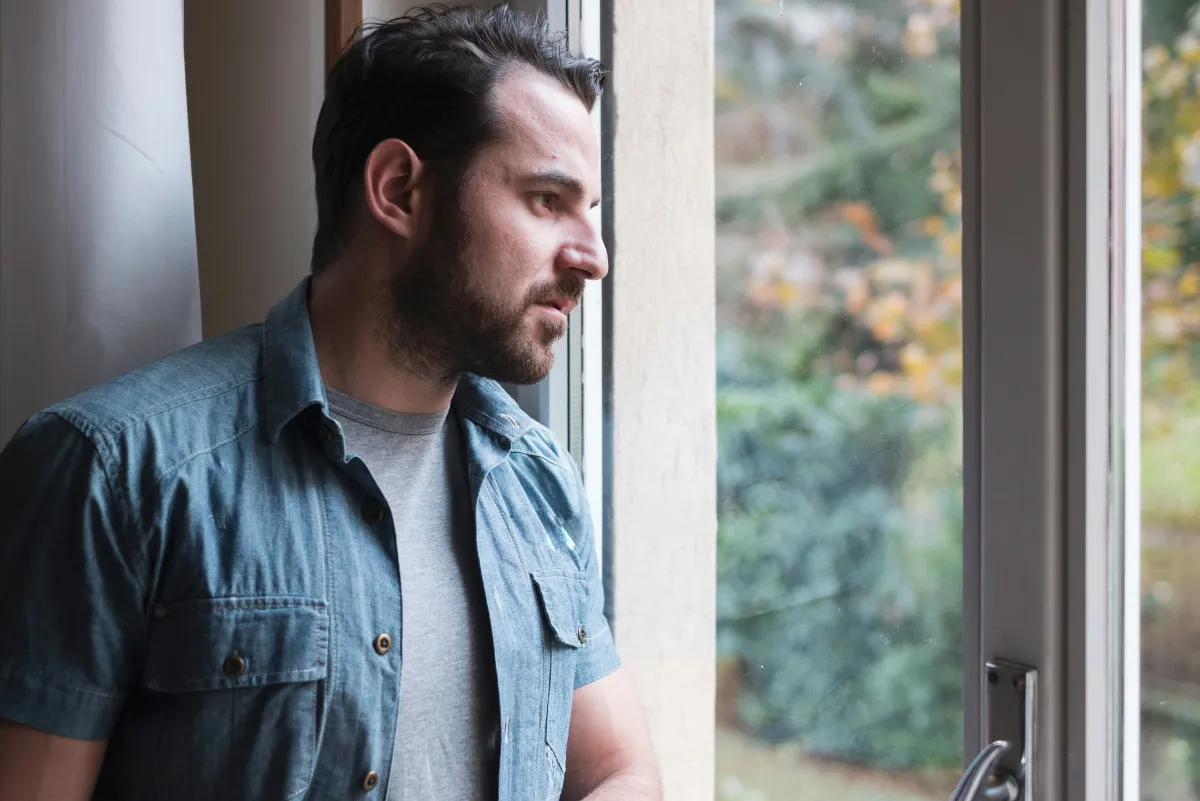 Young man sitting by a window at home, looking outside