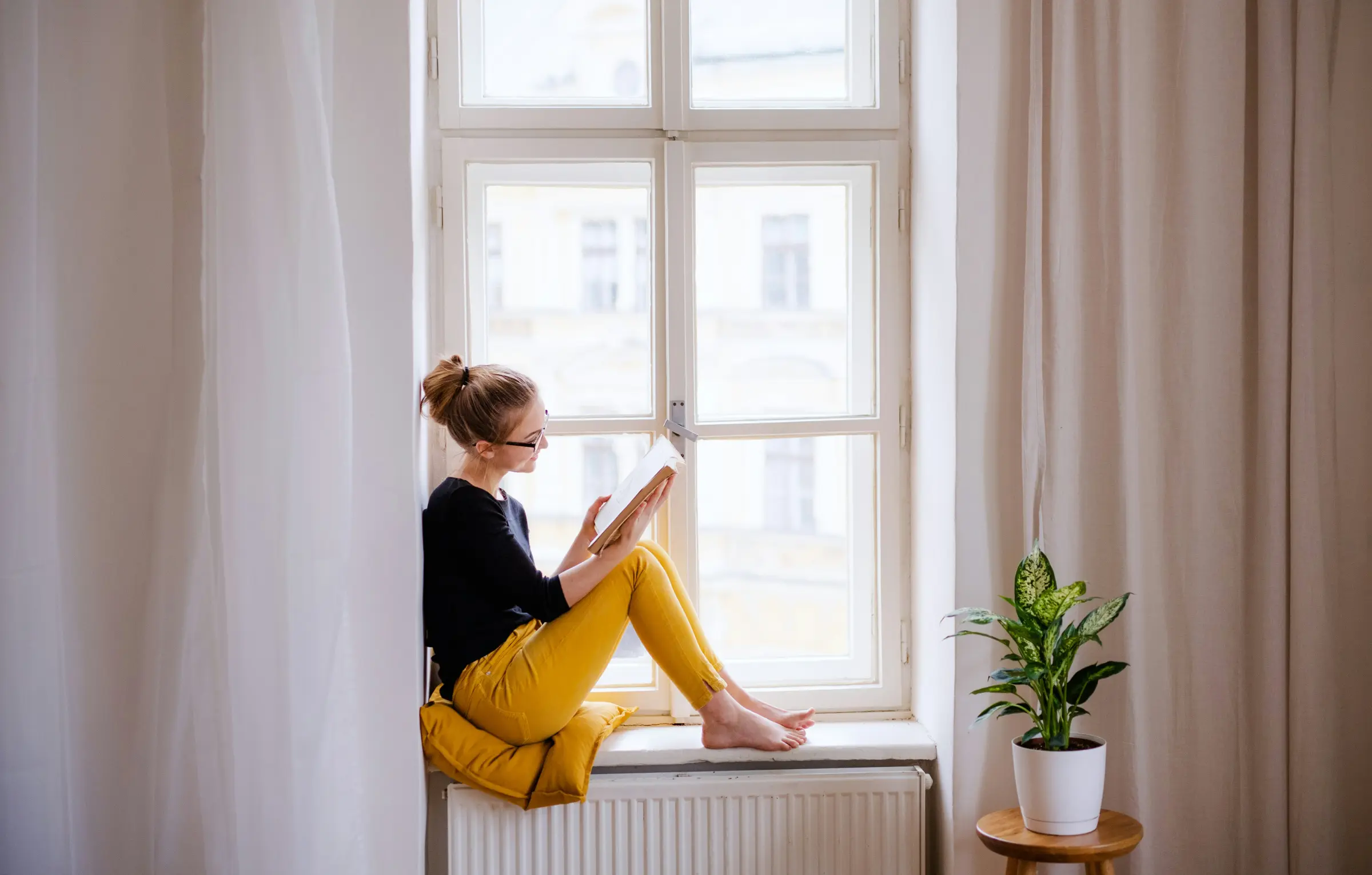 Woman reading a book on a sunny windowsill at home
