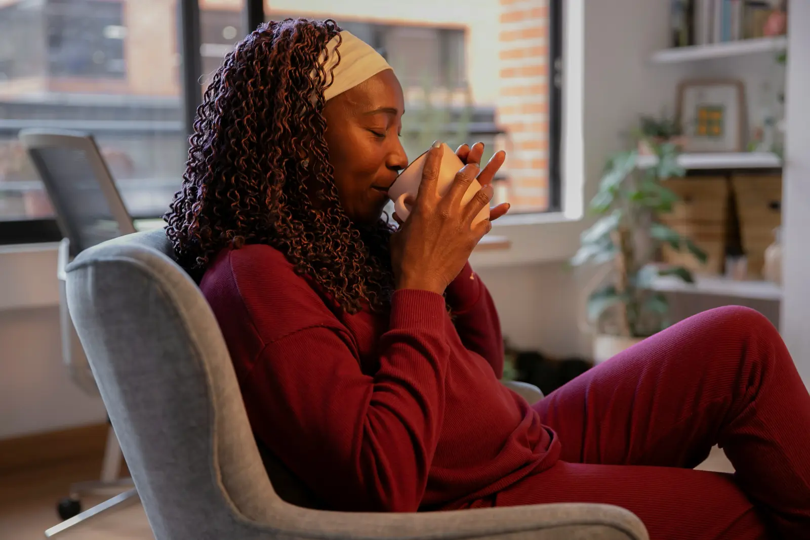 Woman sipping from a mug in an armchair at home