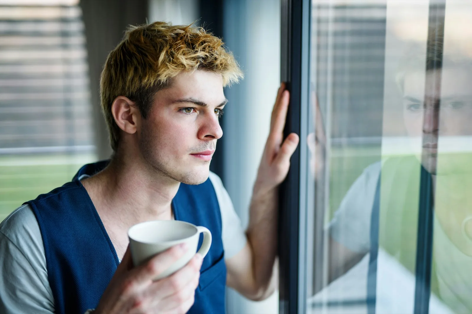 Young adult with a coffee by the window at home