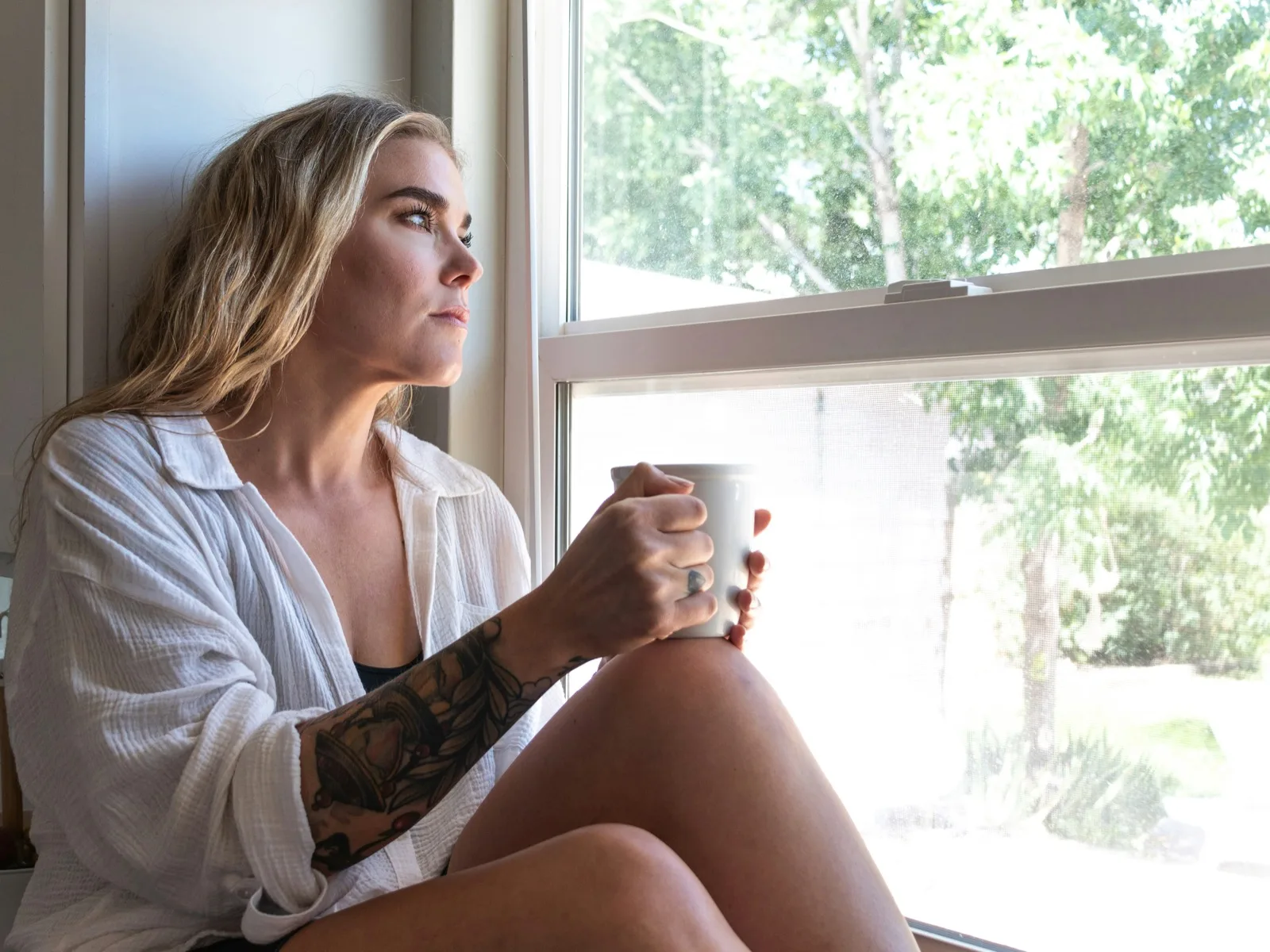 Young adult on a window sill at home with a cup of coffee