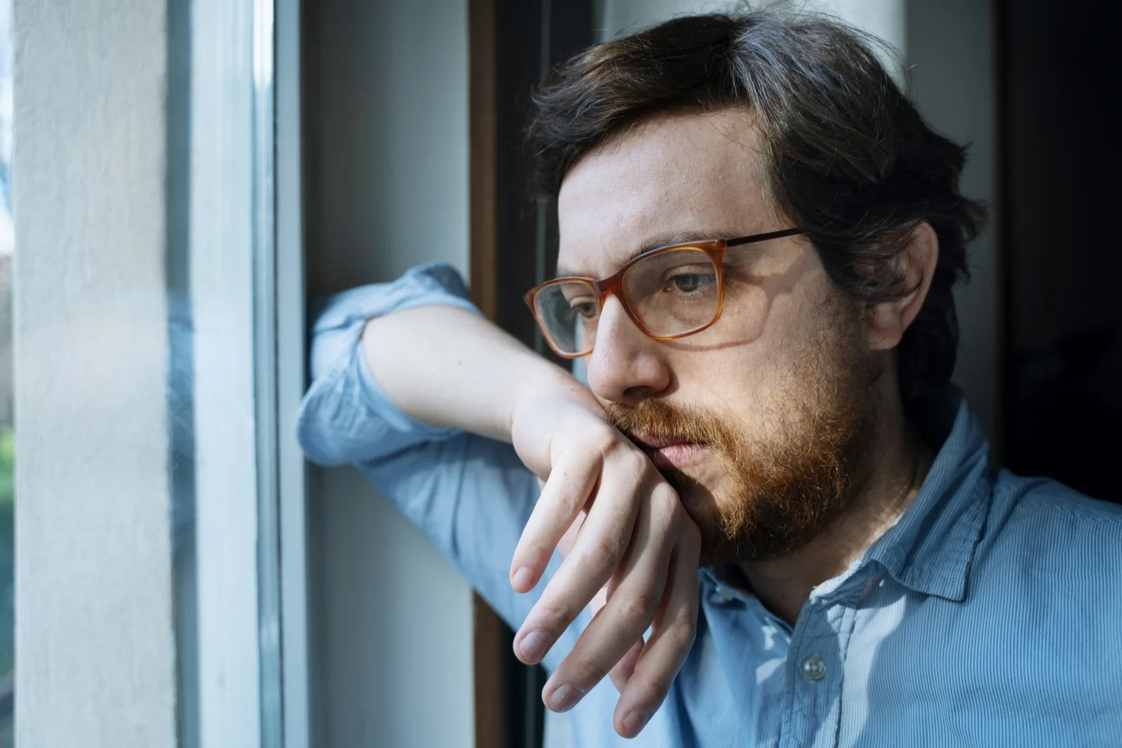 Adult in glasses looking out of a window at home