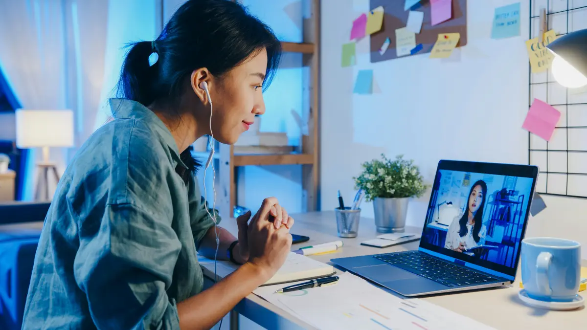 A woman with earphones in a live video session on her laptop at home