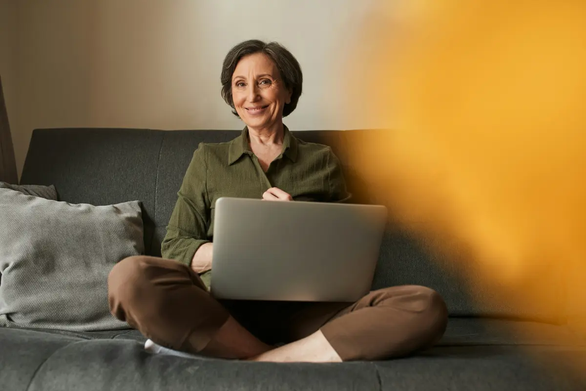 A woman sitting cross-legged on her sofa with a laptop