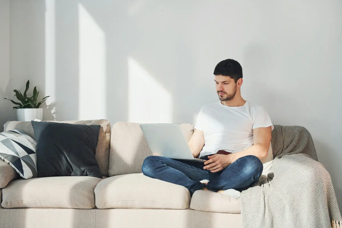 A man with his laptop in a bright bedroom at home