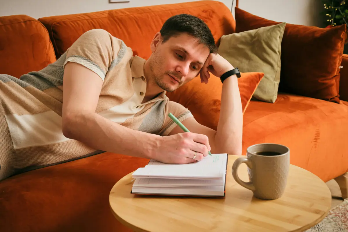 A man writing in a notebook at home with a cup of coffee