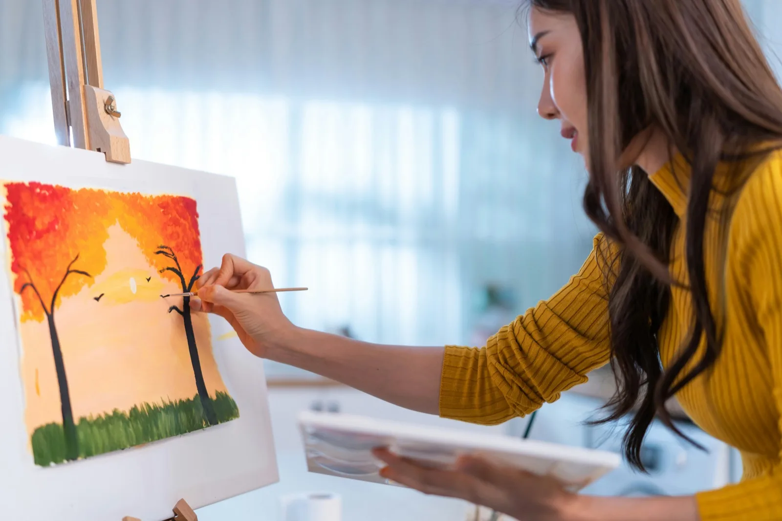 Young adult painting at an easel by the window