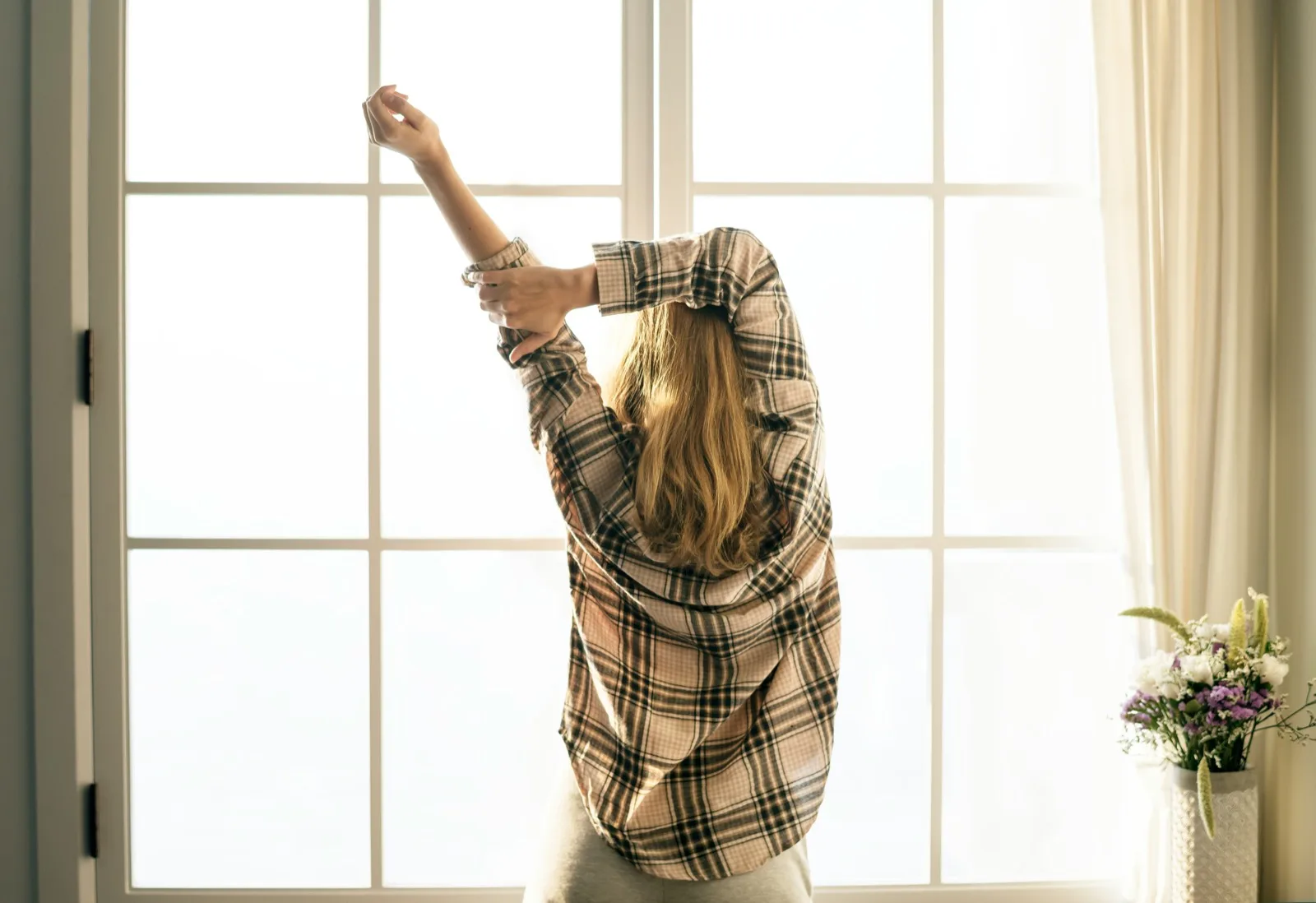 Young adult stretching in the morning light by a window